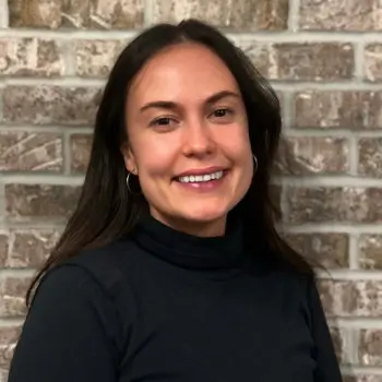 Elina Mukmineva, RDN, LDN – a woman with long dark hair wearing a black turtleneck, smiling in front of a brick wall